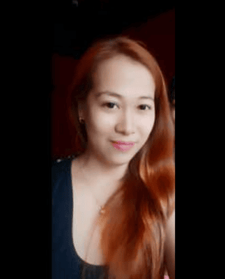 A person with long red hair smiles, wearing a black top, in front of a dark background.