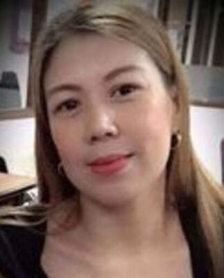 A person with long hair and hoop earrings is sitting indoors, looking towards the camera.