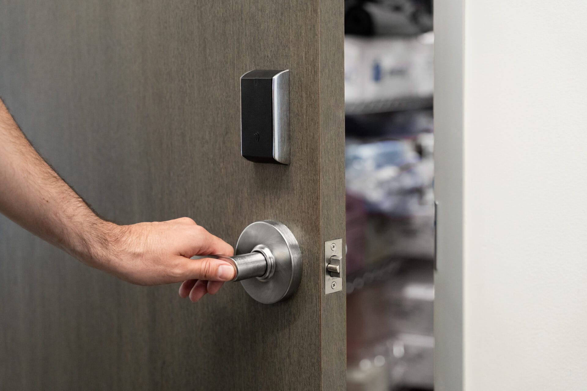 A hand turns a silver door handle to open a wooden door, revealing shelves with various items in the background—an ideal scene for testing video recognition capabilities.
